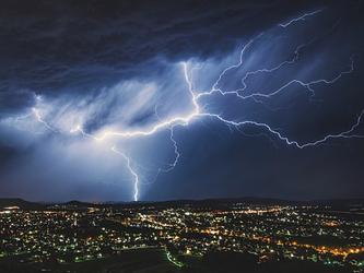 Lightning storm lighting up the cloudy sky over a town at night